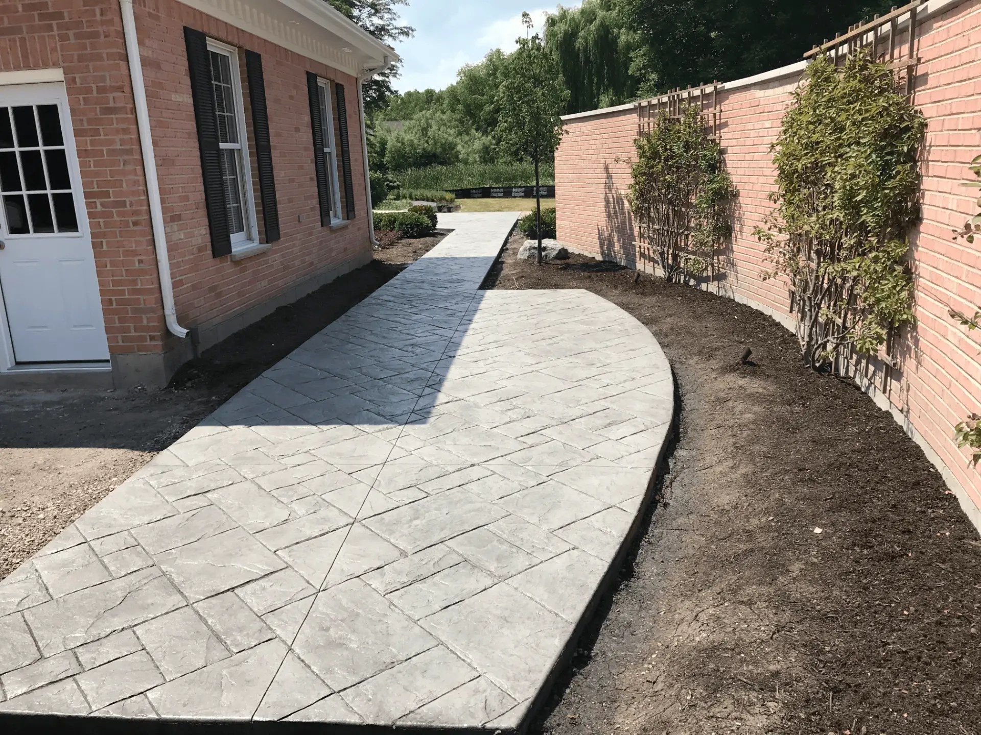Curved stamped concrete walkway between brick walls and fresh landscaping