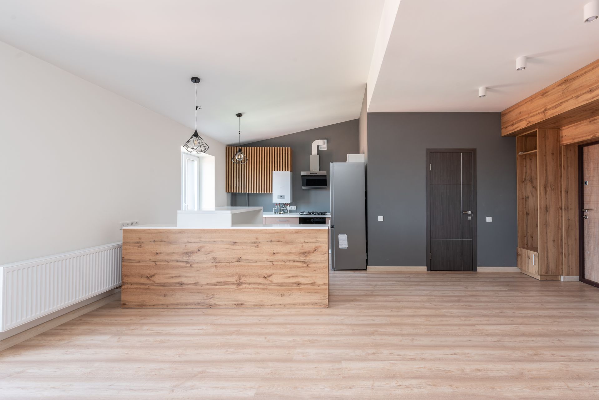 Open-plan interior addition with wood-front island, ribbed wood cabinetry, gray accent wall, and pale oak floors