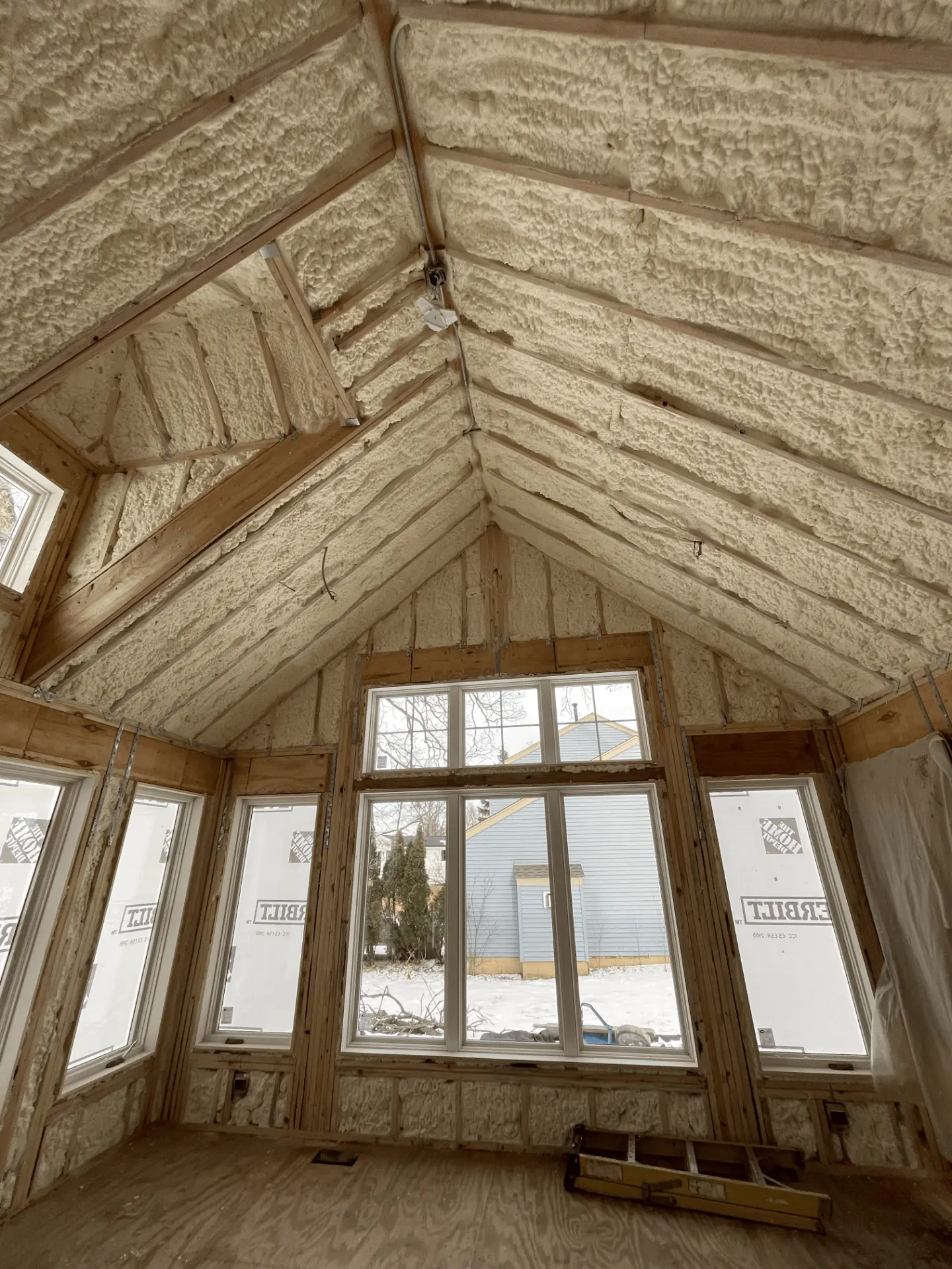 Vaulted room during construction, exposed framing and spray foam insulation behind new windows