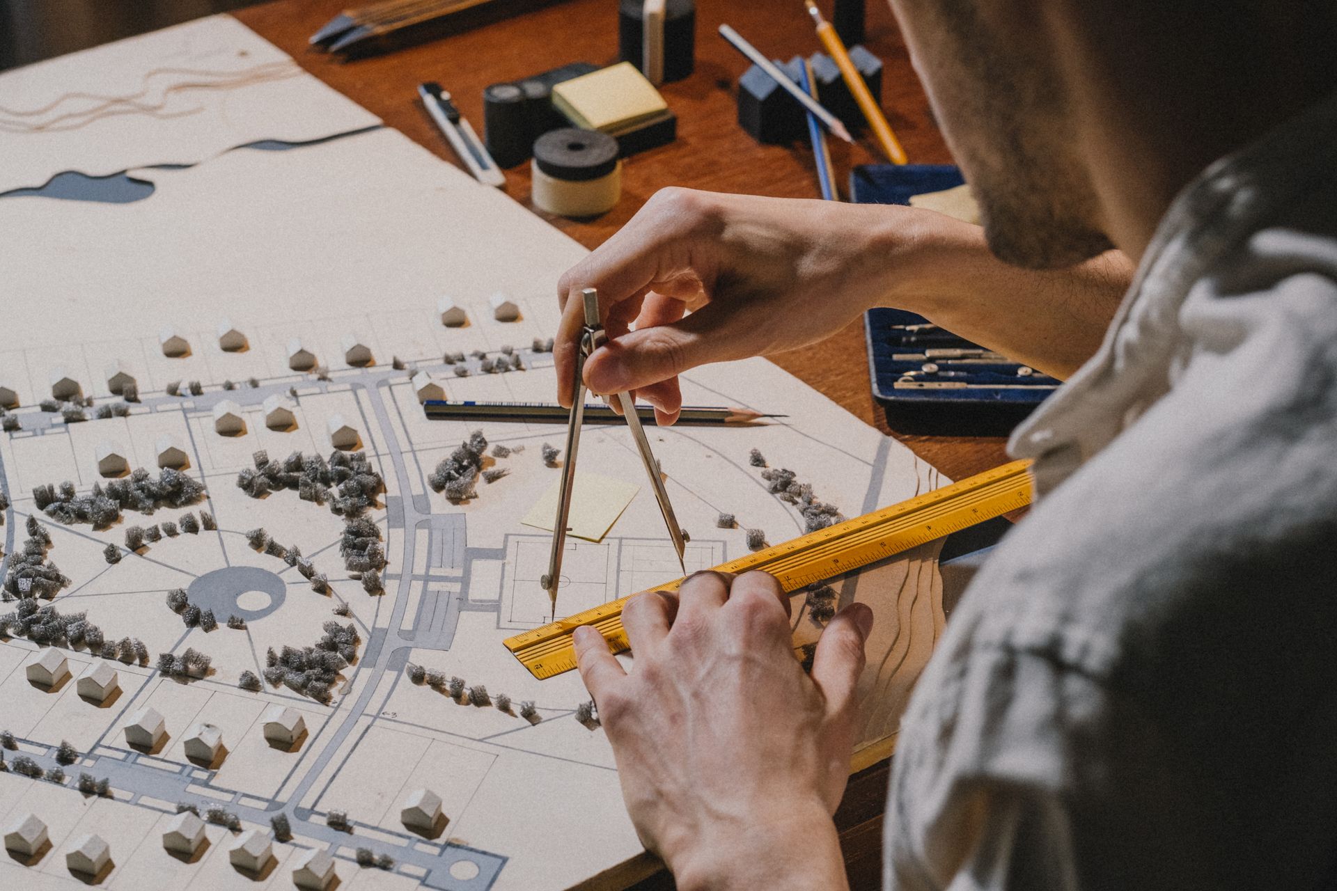 Architect drafting plans with a compass and ruler over a site model