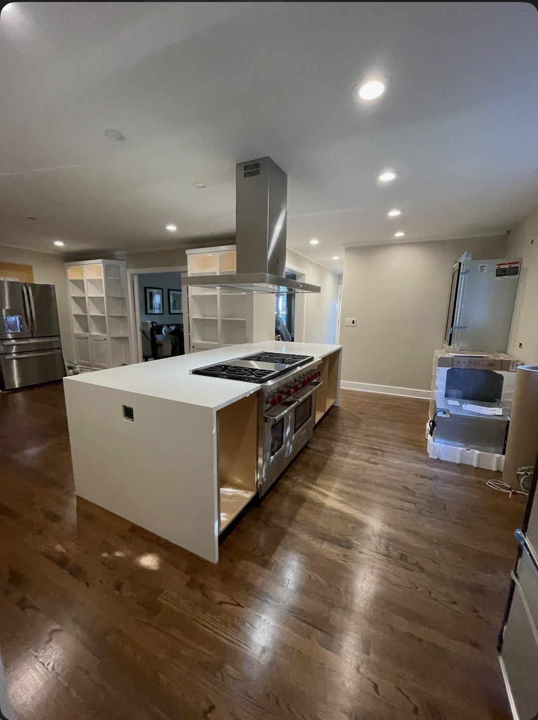 Kitchen island under installation with a waterfall countertop, range hood, and open cabinet frames