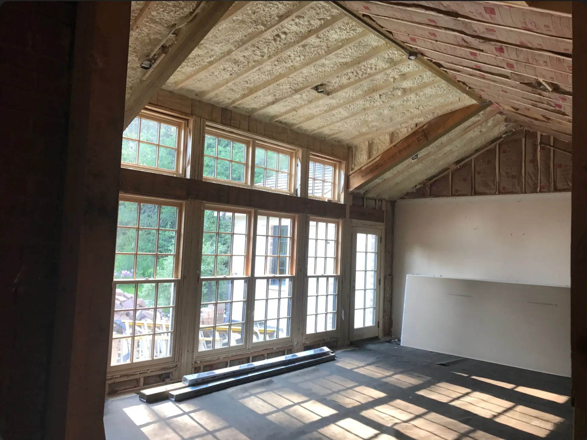 Sunroom under construction with exposed timber framing, roof insulation and large multi-pane windows before drywall