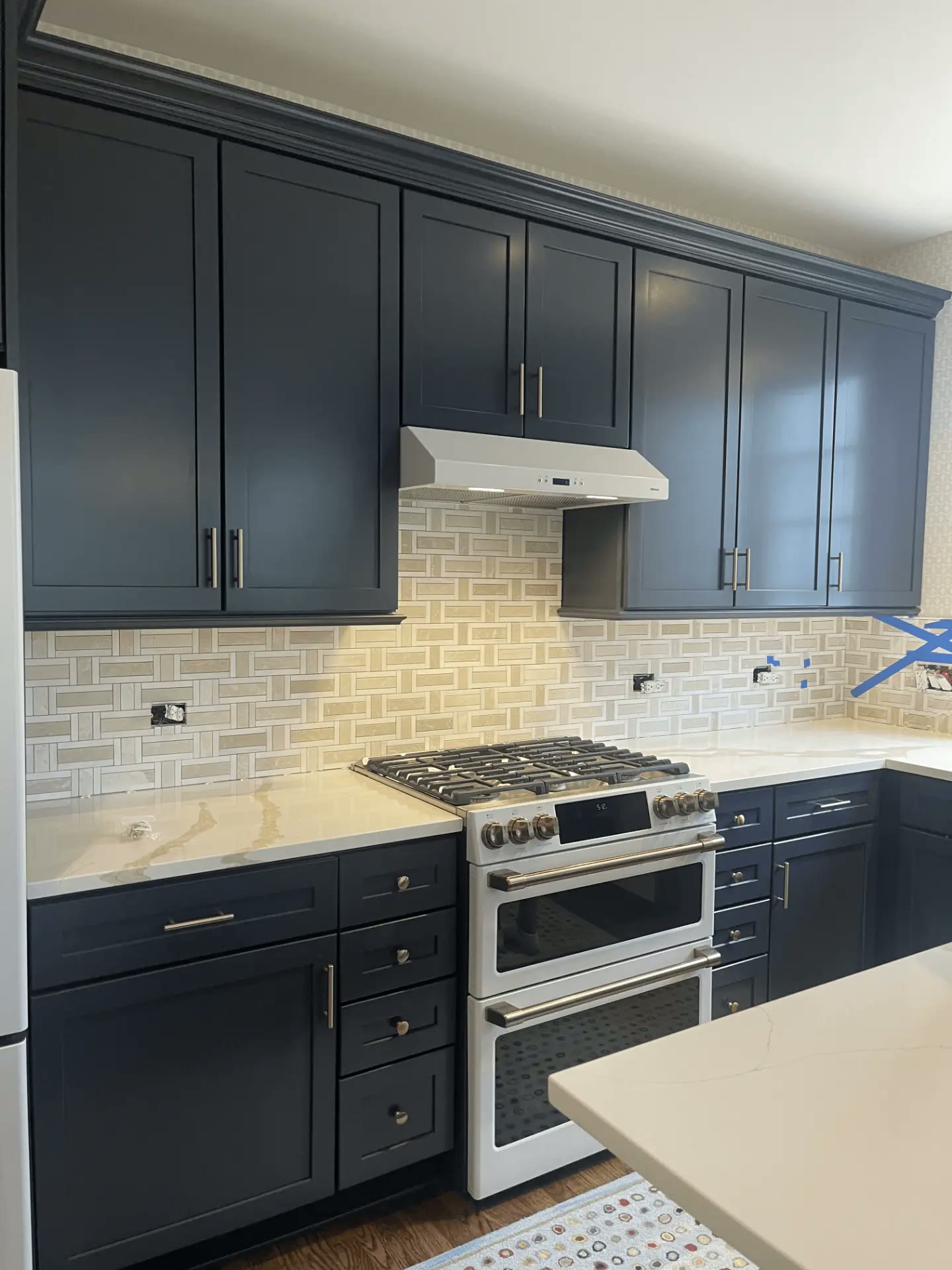 Renovated kitchen with navy cabinetry, stone backsplash, and stainless range