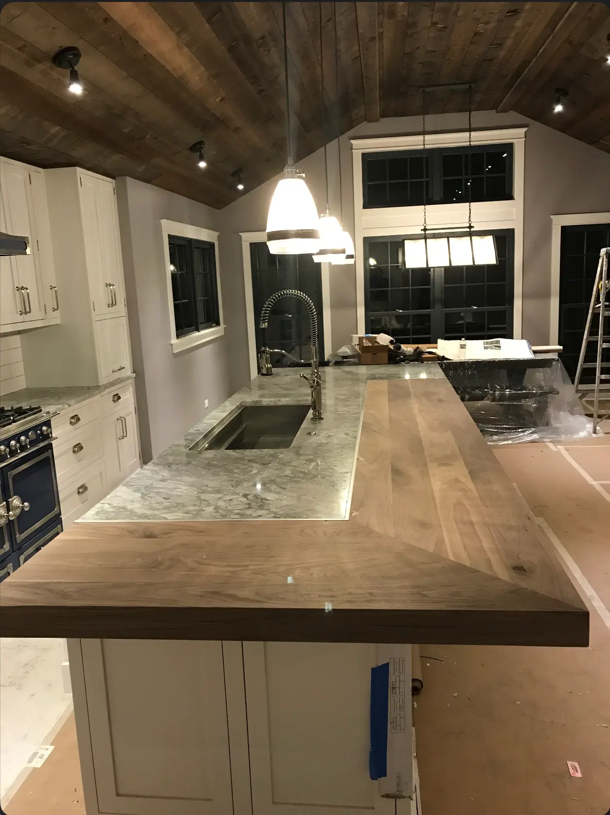 Renovated kitchen with vaulted dark timber ceiling, white cabinetry, marble counters, and a wide wood island