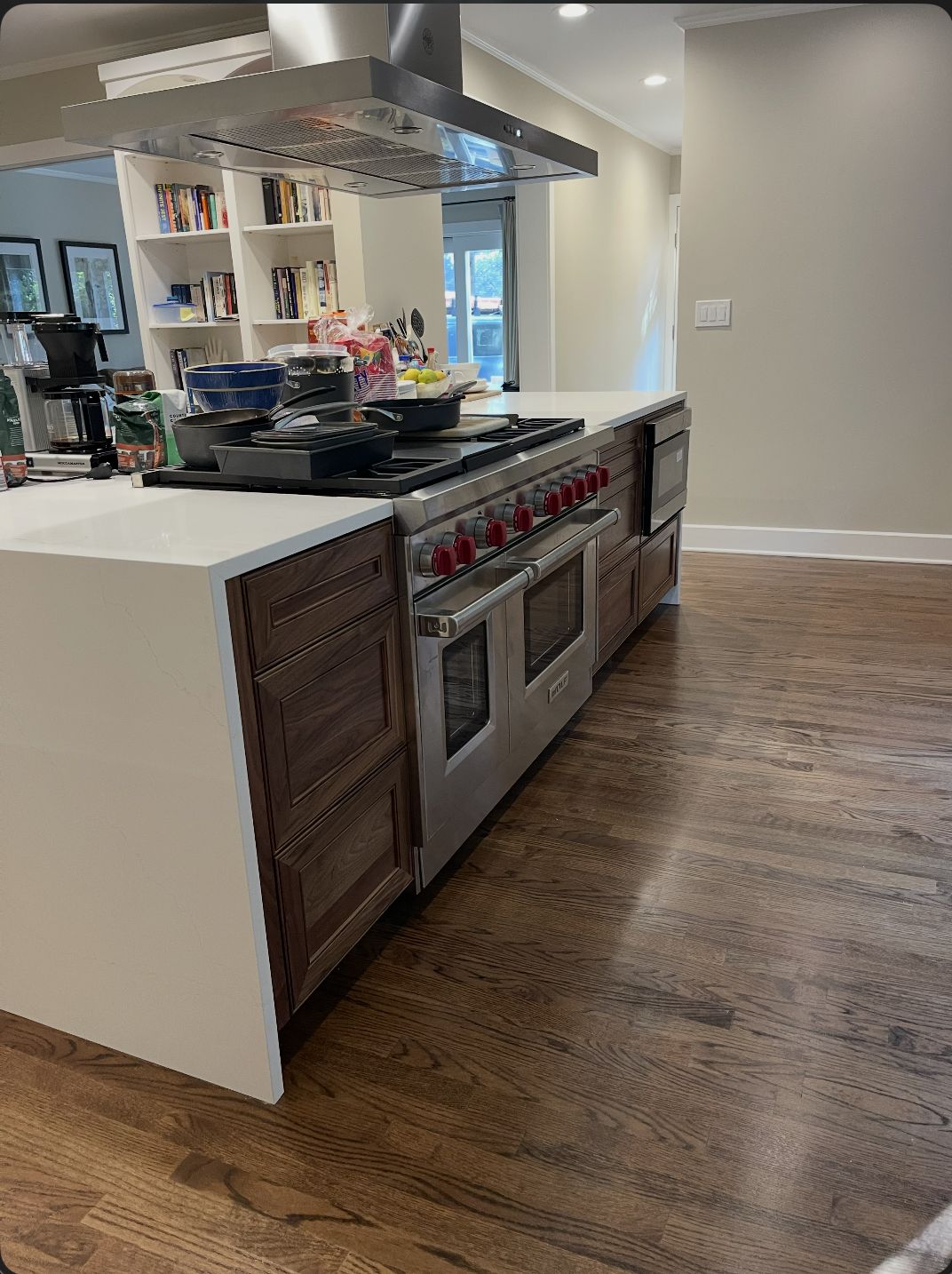 Kitchen island in dark wood cabinetry with a white quartz waterfall top and an integrated range on hardwood floors