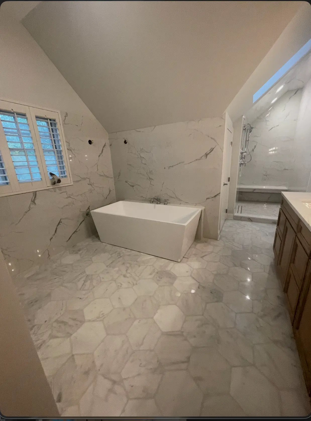 Primary bath with hexagonal marble floors, marble wall slabs, a freestanding soaking tub and a curbless shower