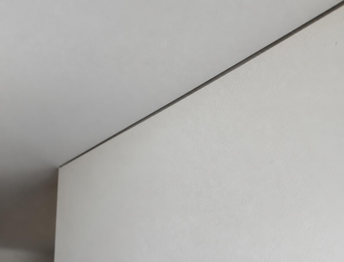 Close detail of a flush reveal where a wall meets the ceiling, with no trim